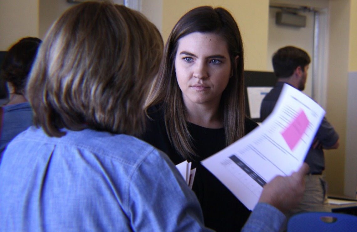 young female, dark blonde hair, speaking to another female